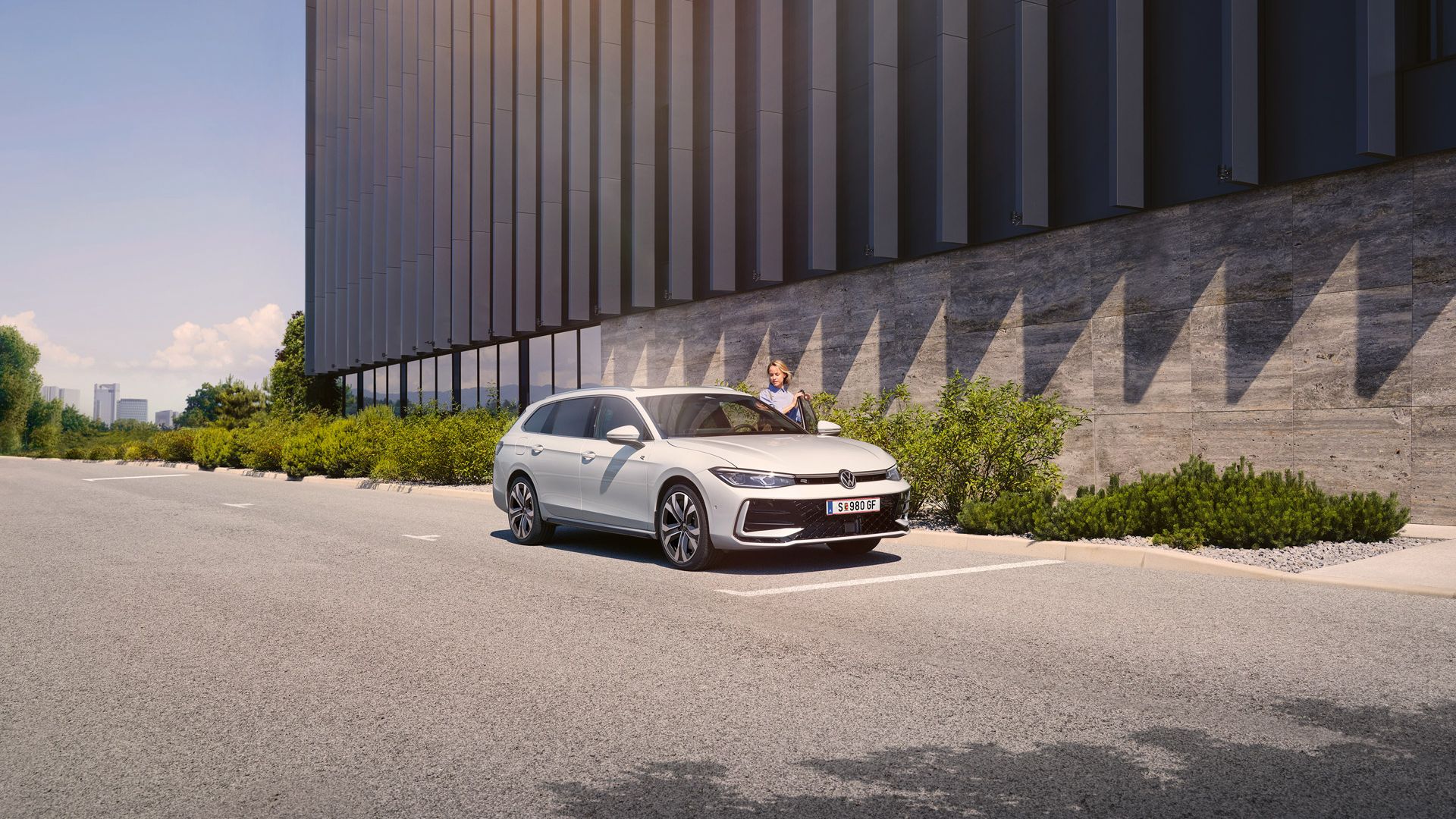  Eine Frau öffnet die Fahrertür eines weißen VW Passat R-Line und steigt ein. Im Hintergrund sieht man ein Gebäude.