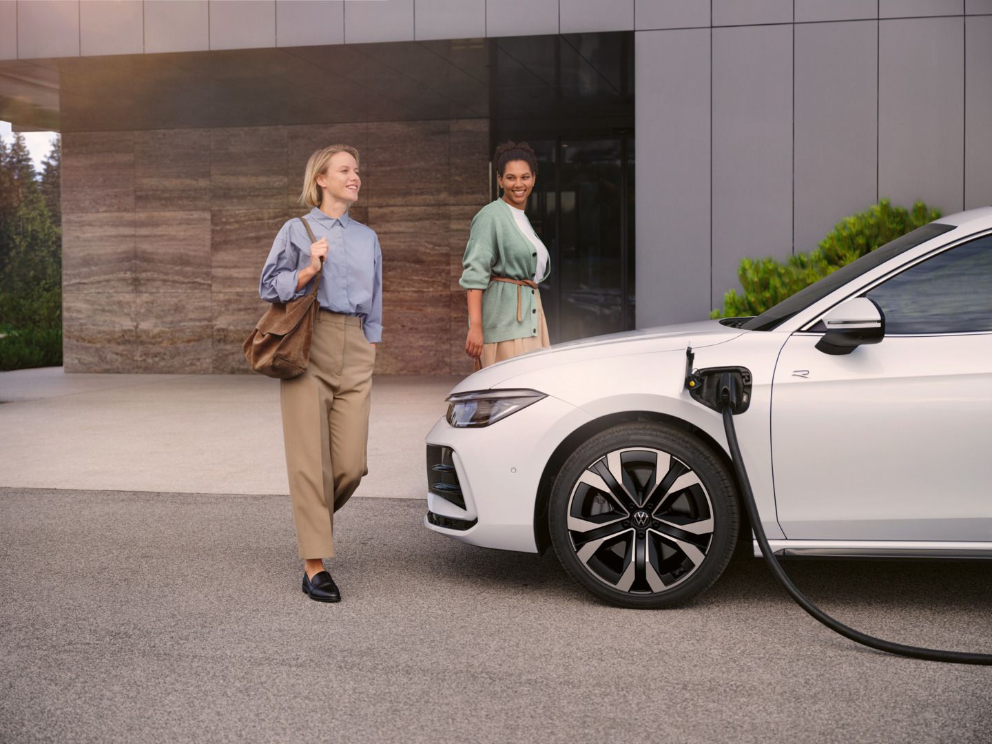 Zwei Frauen gehen auf einen weißen VW Passat R-Line eHybrid zu, der gerade geladen wird.