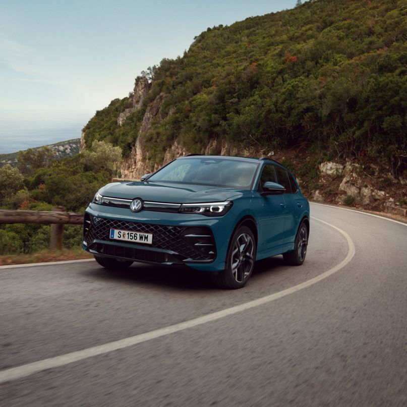  Ein blauer VW Tiguan R-Line eHybrid fährt auf einer kurvigen Landstraße.