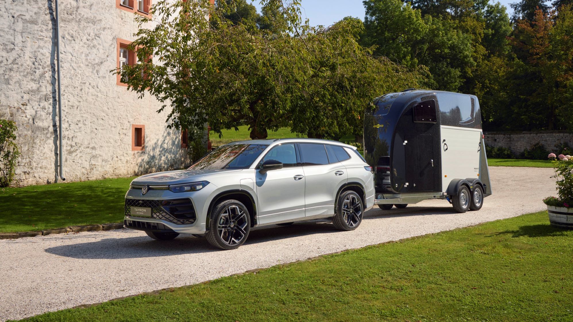 VW Tayron mit Anhänger steht auf einer Straße vor einem Haus.