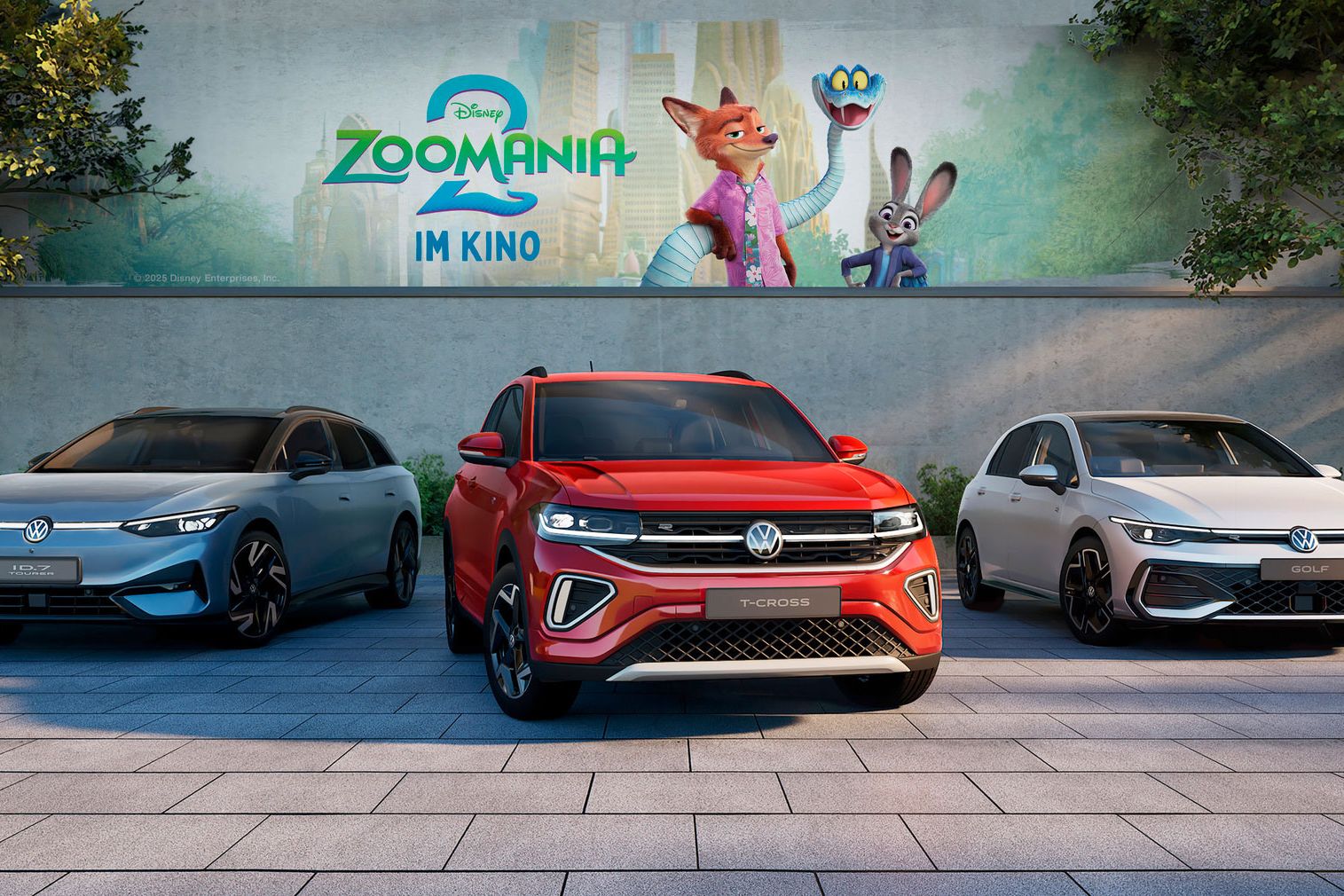 Drei Volkswagen-Fahrzeuge sind nebeneinander auf einem gepflasterten Parkplatz abgestellt. Im Hintergrund ist ein großes Plakat für den Film "Zoomania 2" zu sehen.