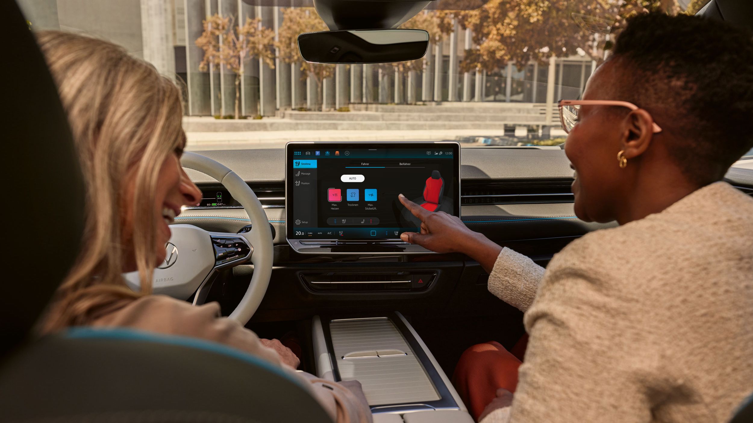 Zwei Frauen, die lachen, sitzen auf den Vordersitzen im VW ID.7 und bedienen das Infotainment-System.