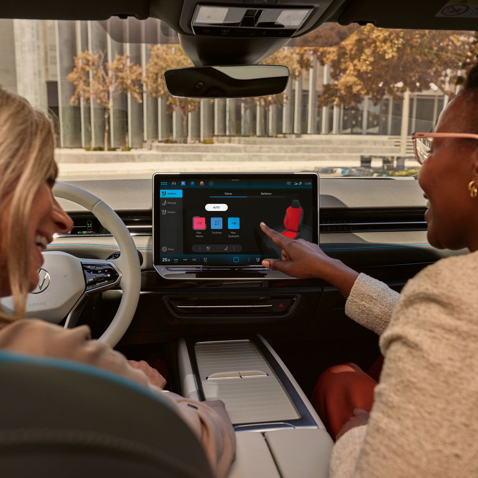 Zwei Frauen, die lachen, sitzen auf den Vordersitzen im VW ID.7 und bedienen das Infotainment-System.