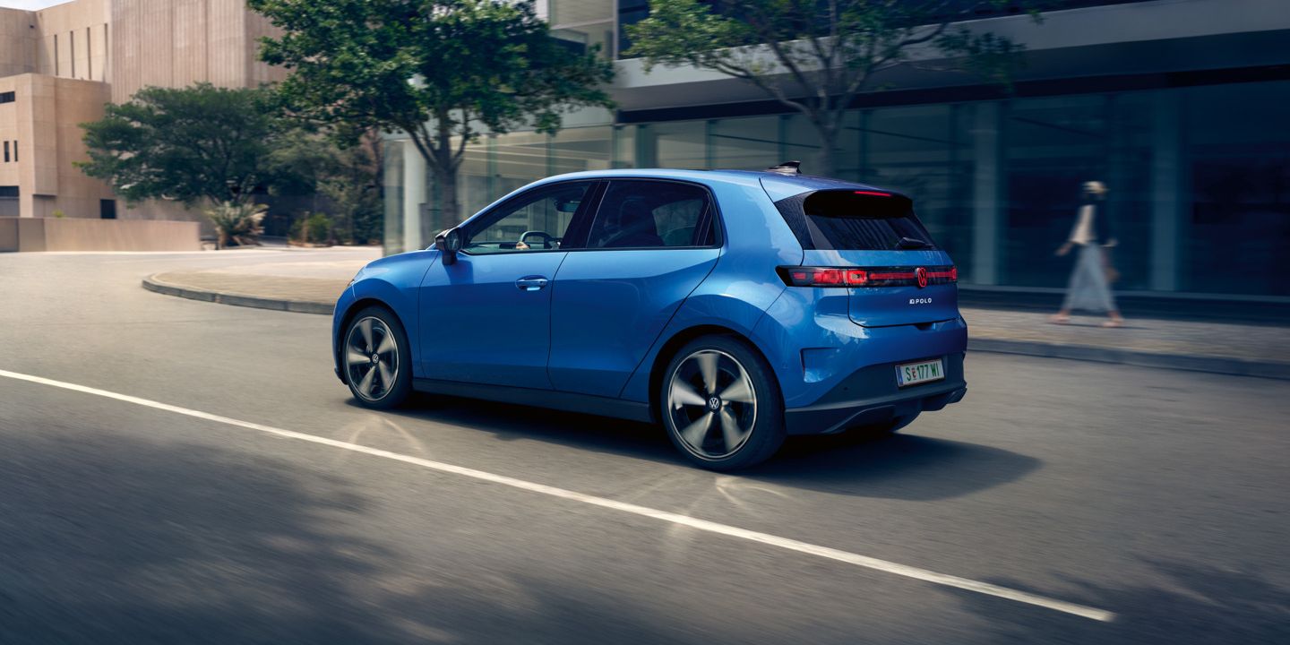 Ein blauer VW ID. Polo Style fährt durch eine Stadt mit grünen Bäumen am Straßenrand.