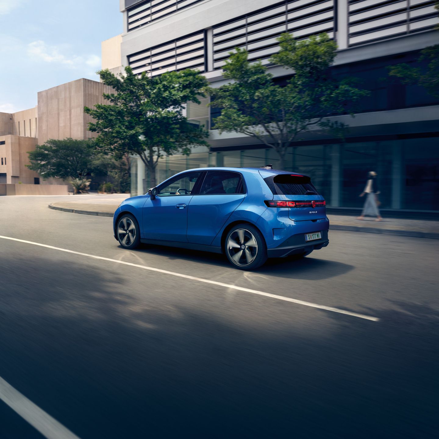 Ein blauer VW ID. Polo Style fährt durch eine Stadt mit grünen Bäumen am Straßenrand.