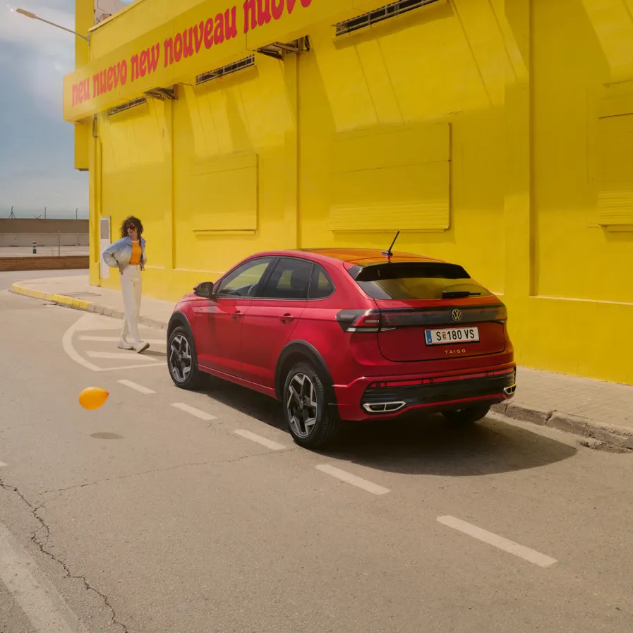 Ein roter VW Taigo steht vor einer gelben Halle am Straßenrand, eine Frau geht darauf zu.