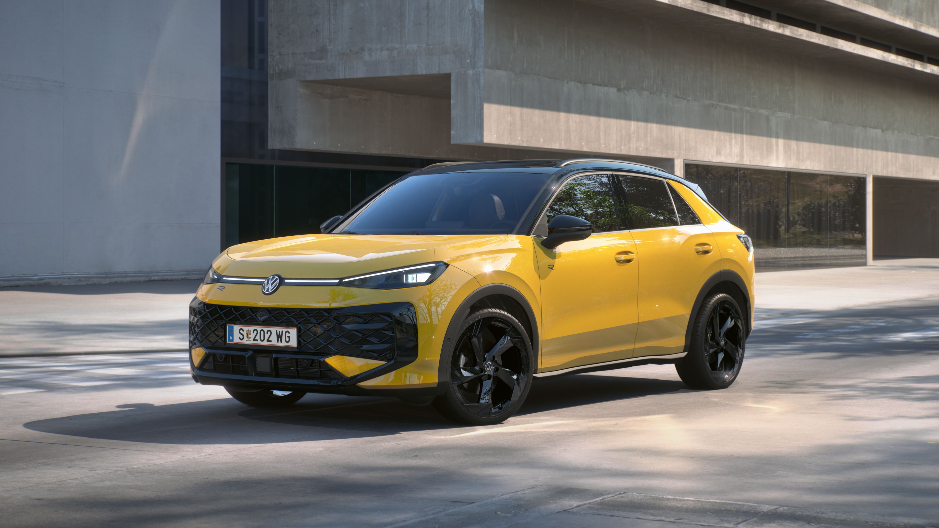 Eine gelber Volkswagen T-Roc R-Line steht in 3/4-Frontansicht vor einem Gebäude.