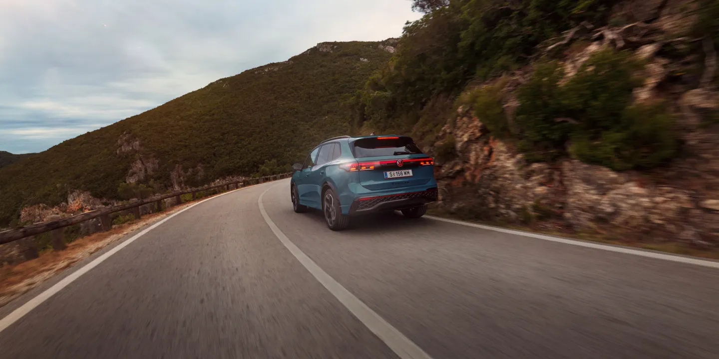 Roter VW Tiguan in Heckansicht fährt durch eine bergige Landschaft.
