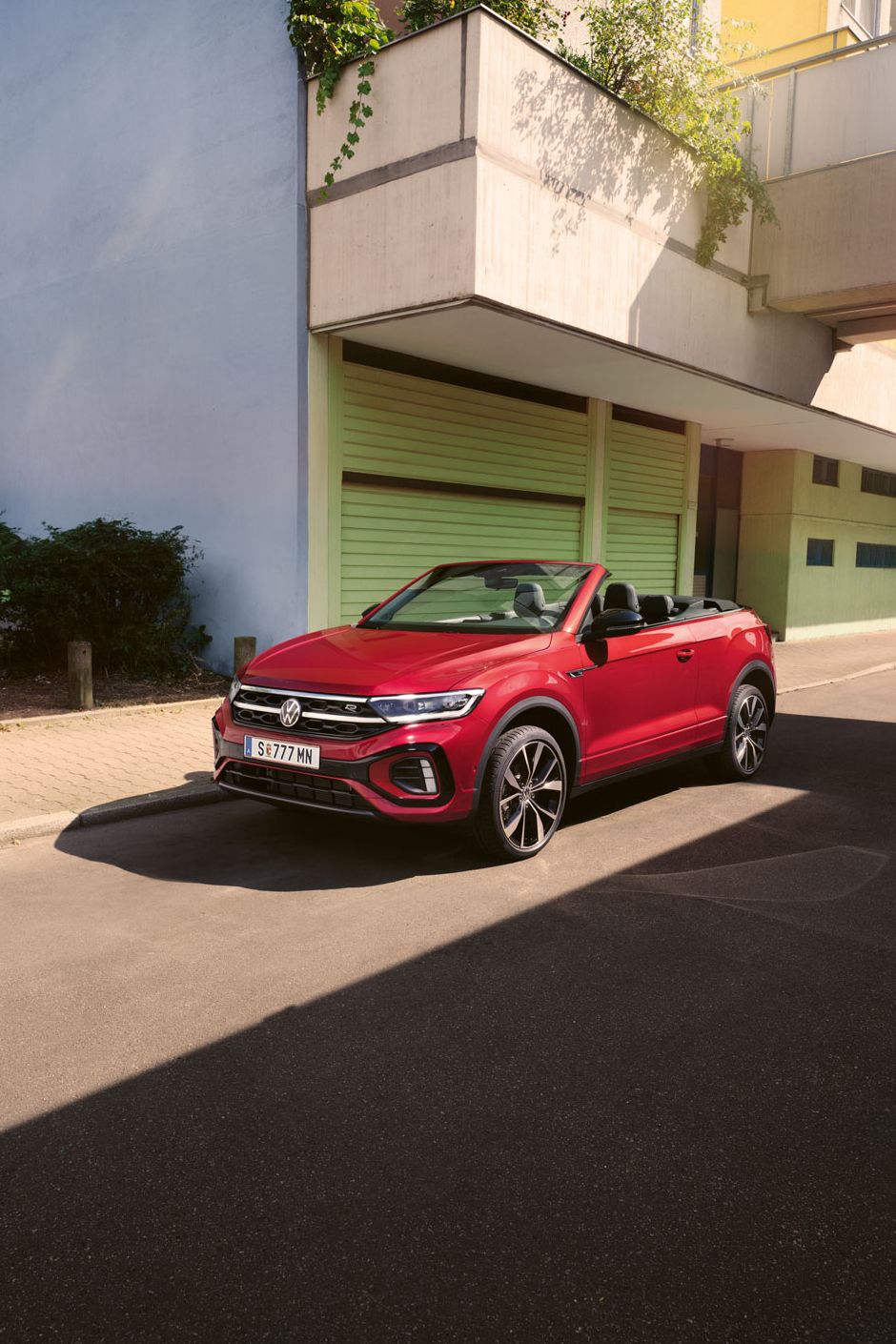 Roter T-Roc Cabriolet steht geparkt am Straßenrand neben dem Gehsteig in einer Stadt.
