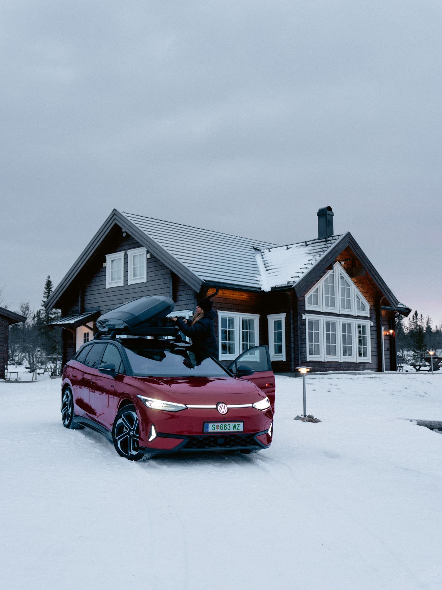 Ein roter ID.7 Tourer GTX mit Dachbox steht im Schnee vor einem Wohnhaus. 