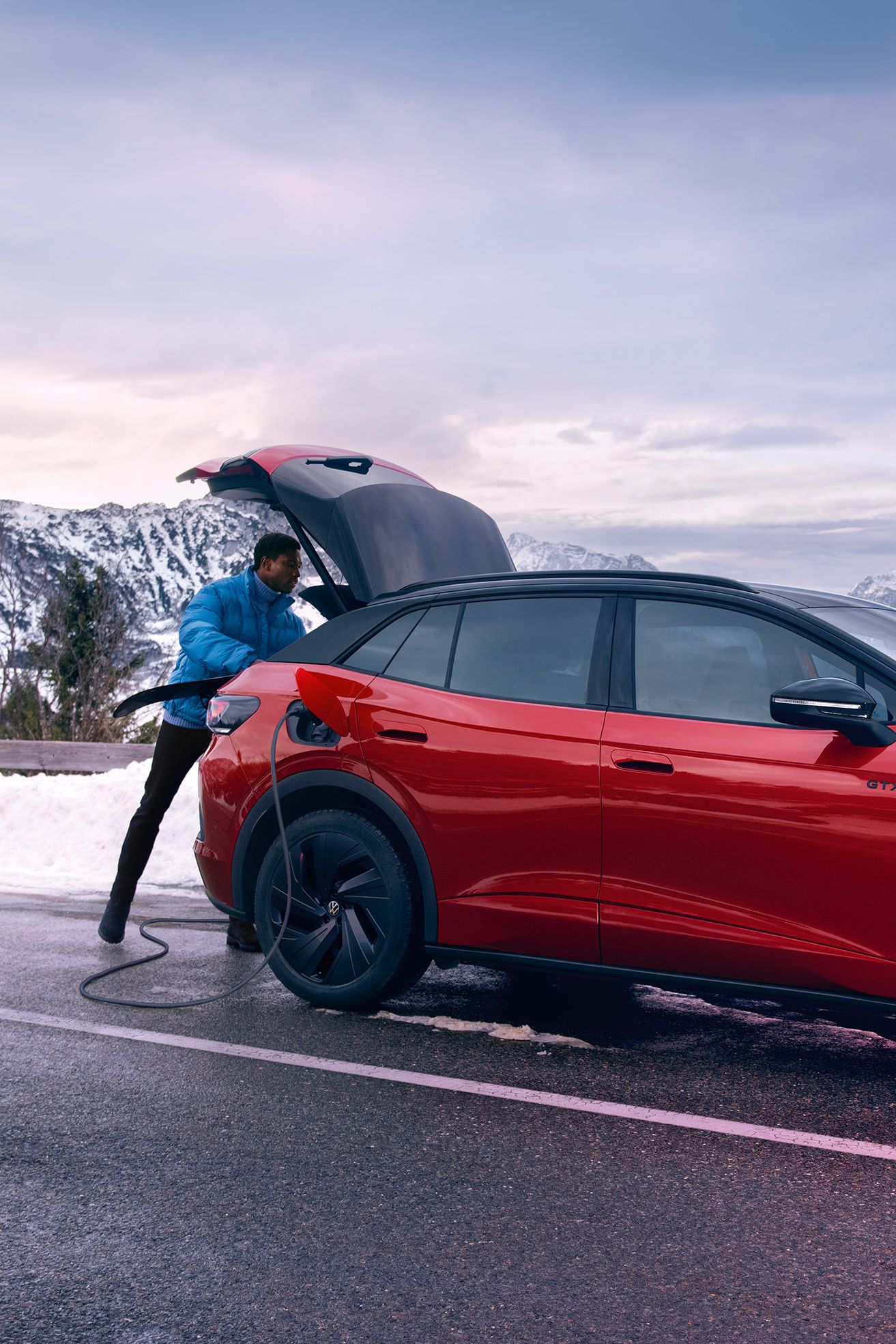 Mann öffnet Kofferraum eines VW ID.4 GTX auf einer Bergstraße