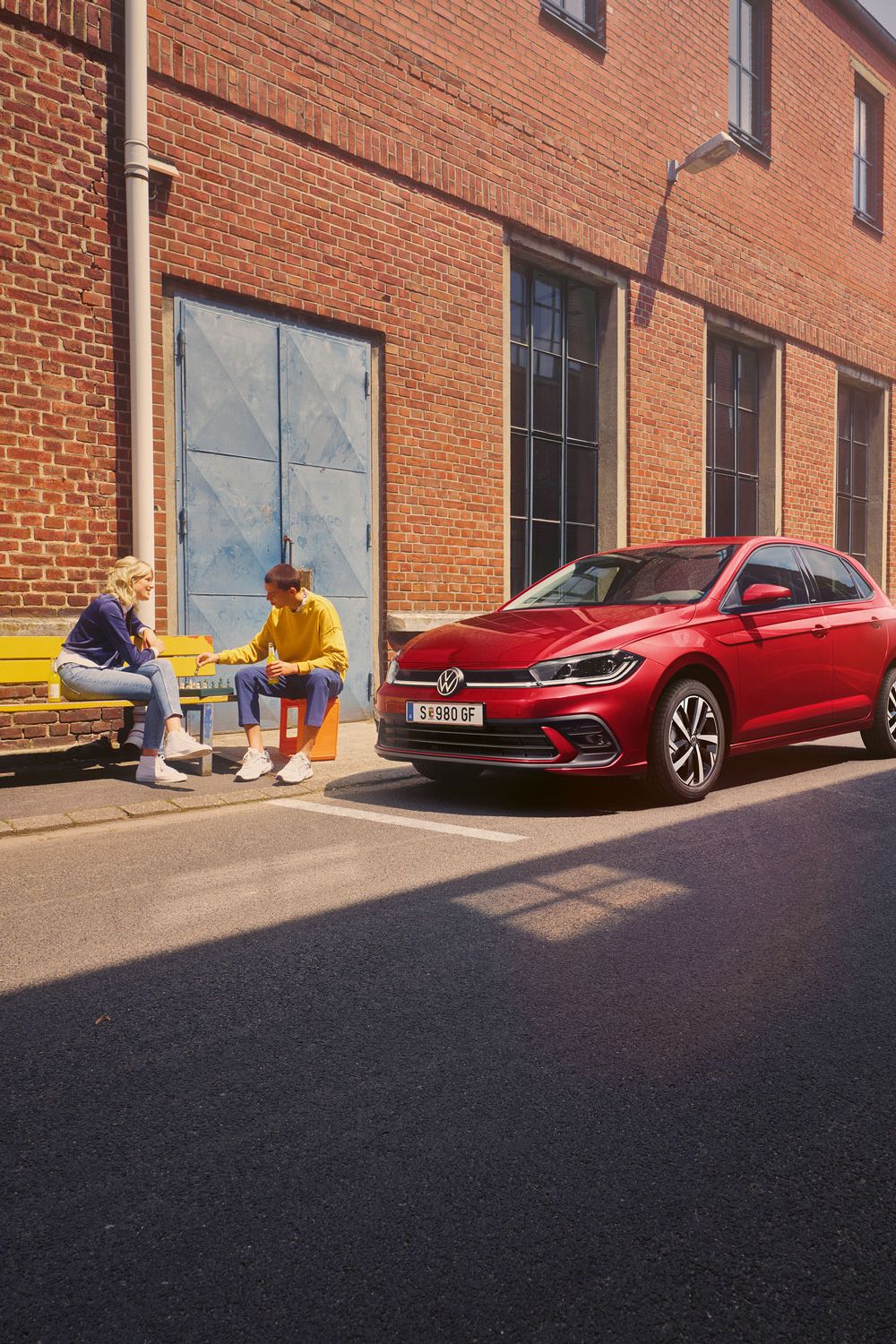 Zwei Personen spielen Schach vor einem roten VW Polo Style, der vor einem Fabrikgebäude parkt.
