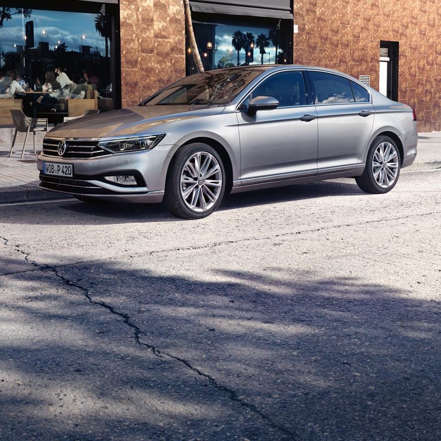 VW Passat steht auf einer Straße vor einem Café mit Sitzmöglichkeiten.