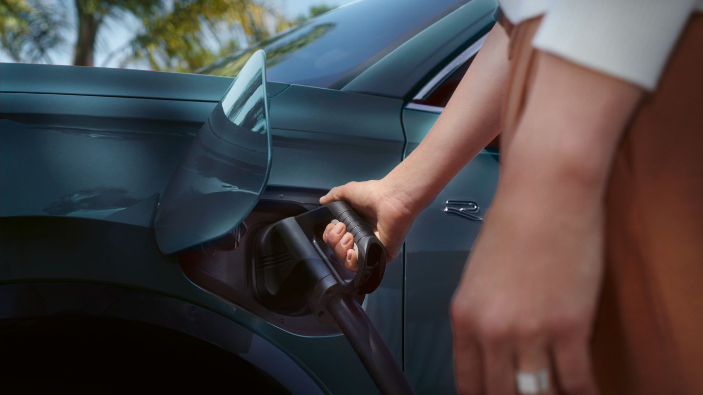 Eine Frau steckt ein Ladekabel in die Ladebuchse eines blauen VW Tiguan eHybrid