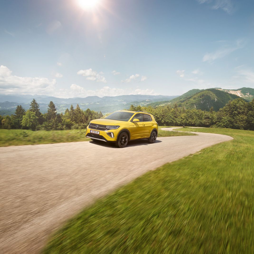 Ein gelber VW T-Cross auf einer Straße in hügeliger Landschaft.