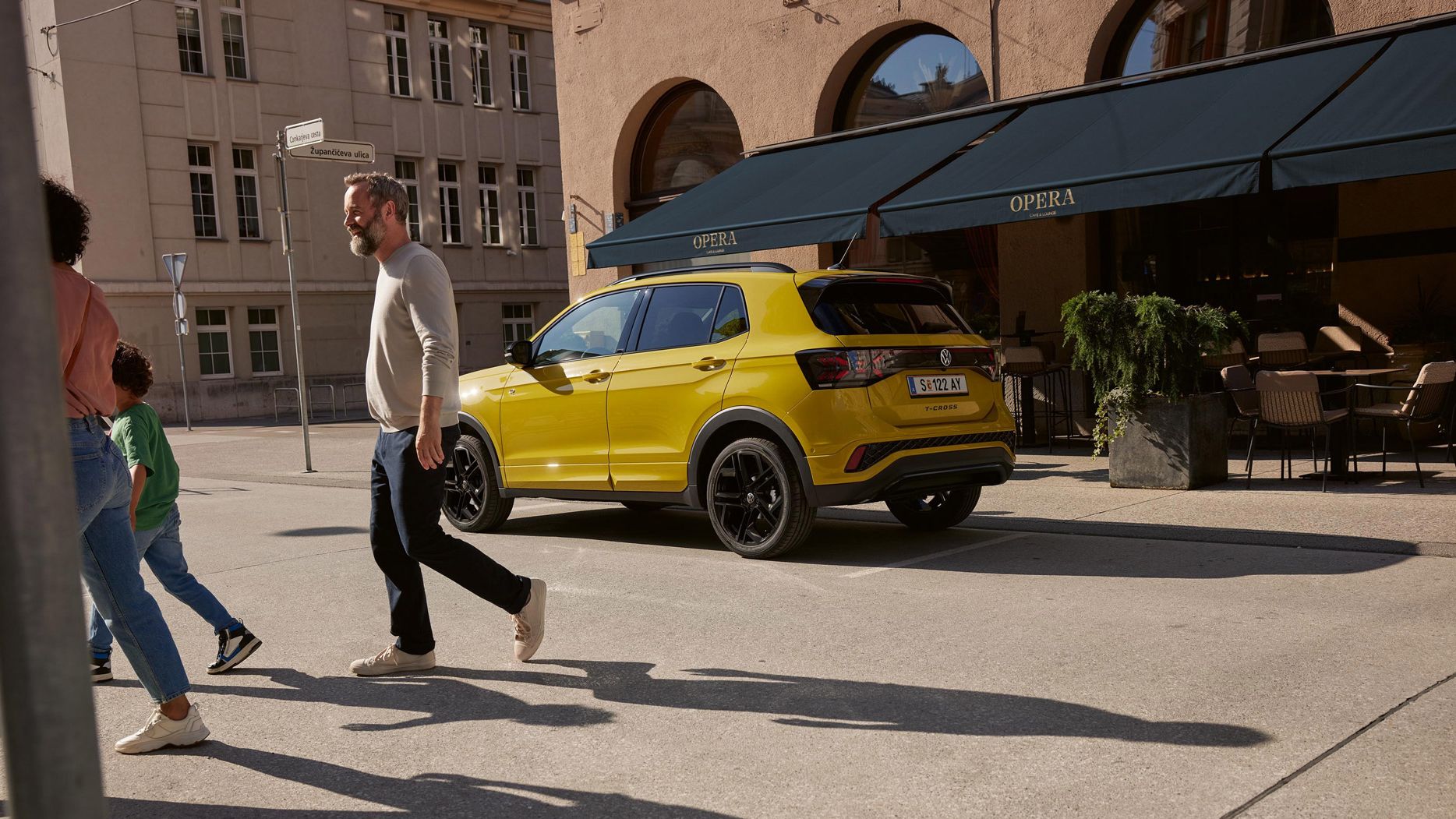 Ein gelber VW T-Cross parkt vor einem Café. Eine Familie geht davor über die Straße.
