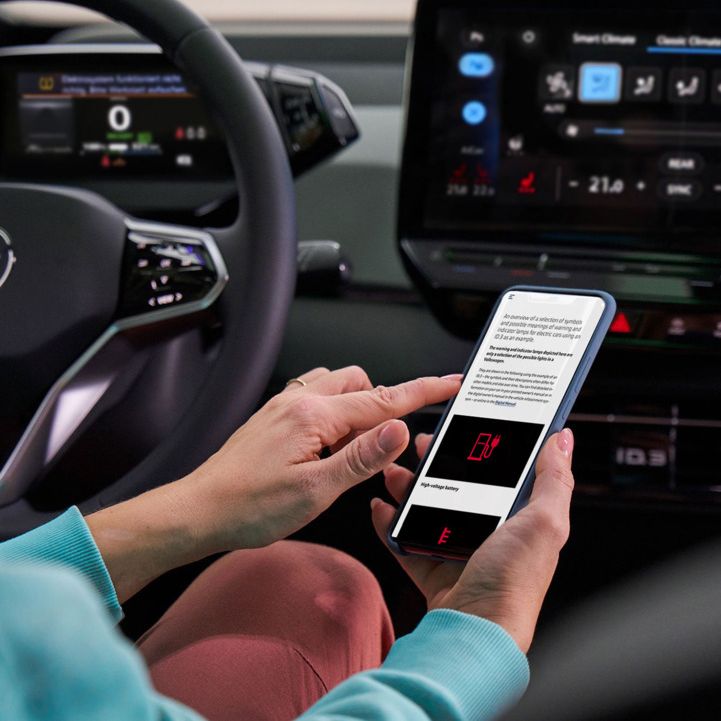 Kundin sitzt am Lenkrad eines VW-Autos und informiert sich über Warnleuchten