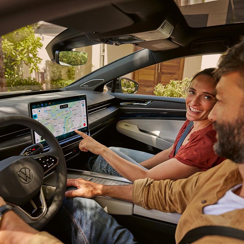 Ein Mann und eine Frau sitzen vorn im VW ID.7, die Frau zeigt auf die Kartenansicht im Infotainment-System.