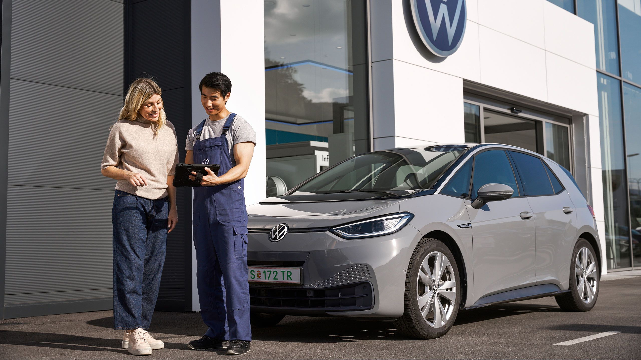 Ein Volkswagen Techniker und eine Kundin stehen vor einem grauen Volkswagen ID.3