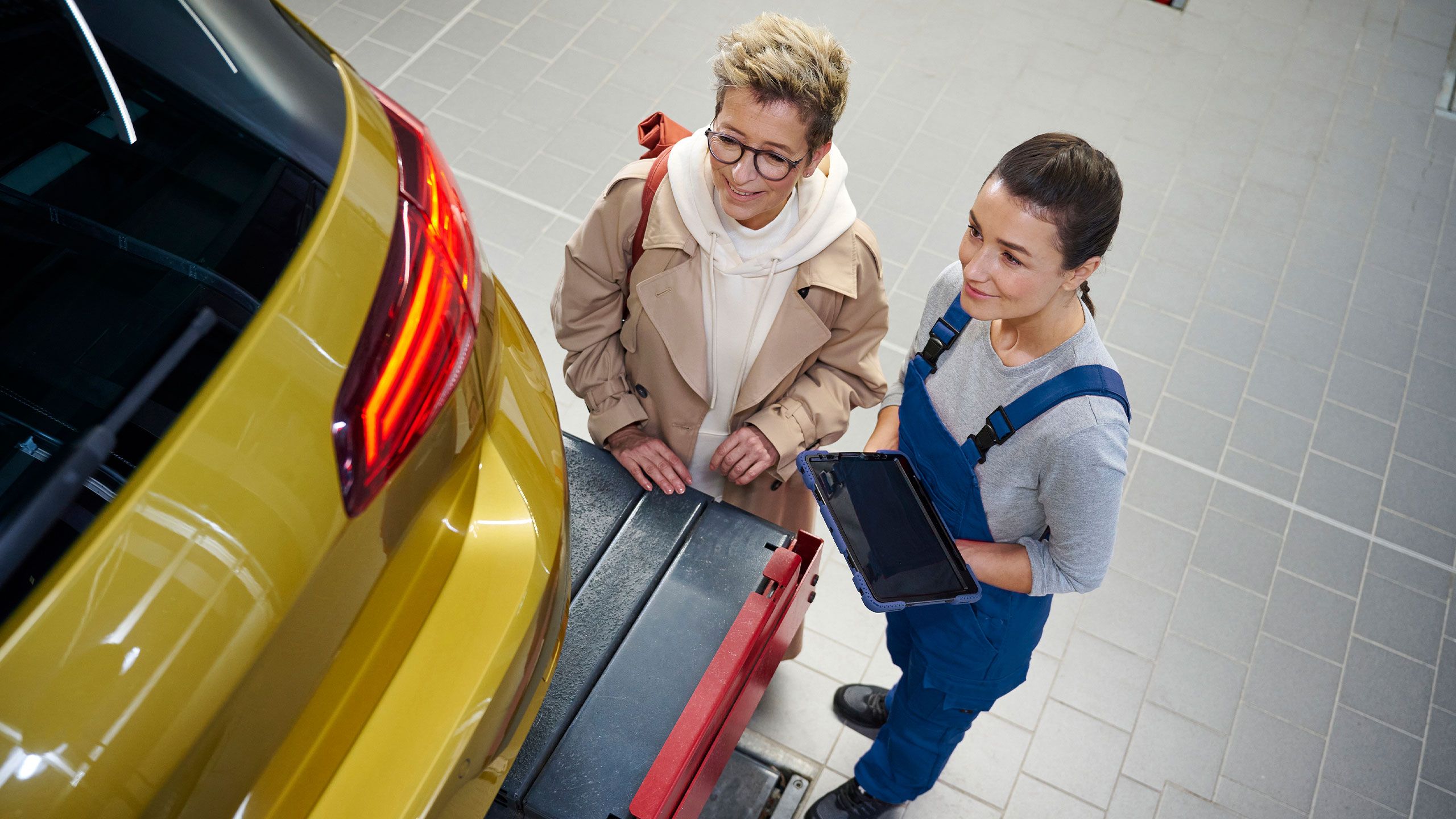 Zwei Personen stehen neben dem Kofferraum eines gelben VW Golf in einer Werkstatt.