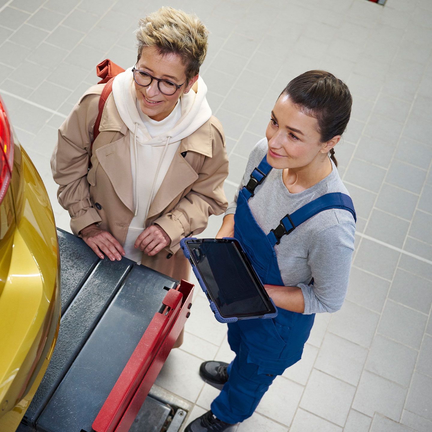 Zwei Personen stehen neben dem Kofferraum eines gelben VW Golf in einer Werkstatt.