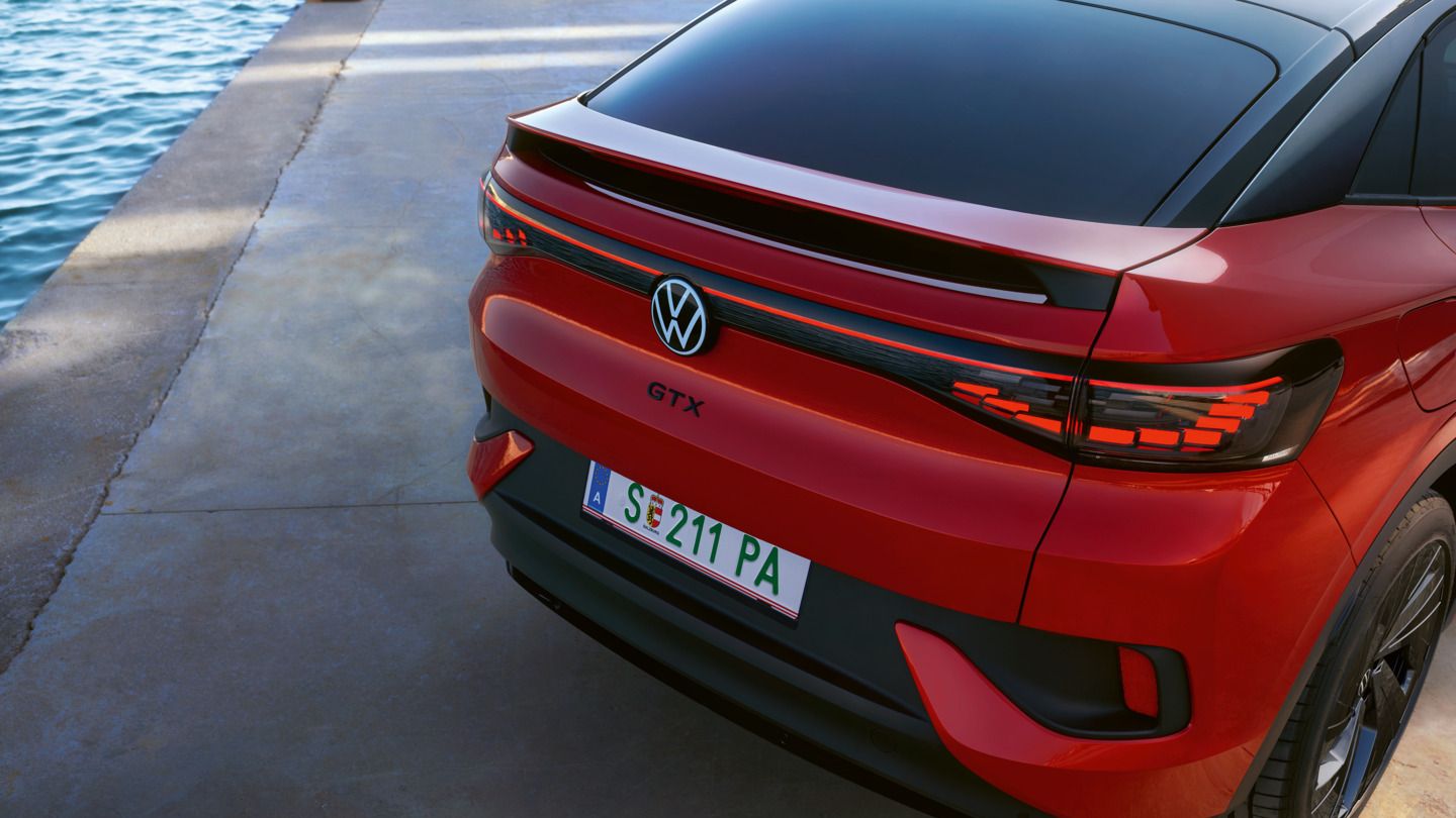 Ein rotes Volkswagen Elektroauto, Modell GTX, steht auf einer betonierten Fläche neben Wasser. Das Auto hat eine italienische Nummernschild und moderne Lichtleisten am Heck.