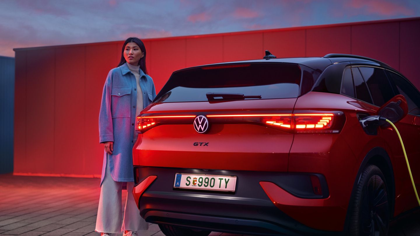 VW ID.4 GTX in Rot von hinten beim Laden. Frau steht daneben.