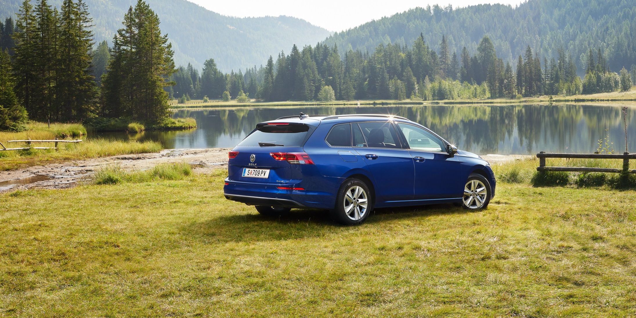Ein blauer VW Golf Variant steht auf einer Wiese vor einem See