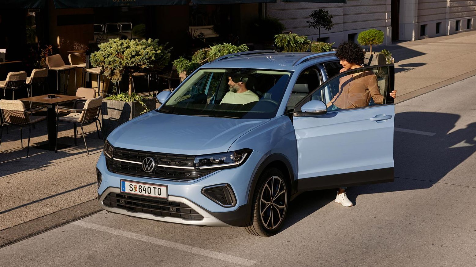 Eine Frau steigt in einen blauen VW T-Cross, der vor einem Straßencafé parkt.