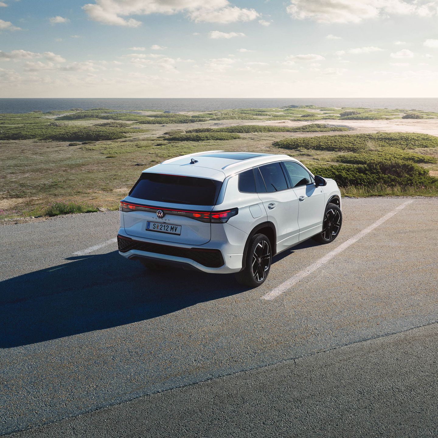 Heckansicht eines weißen VW Tayron auf einem Parkplatz in Dünen.