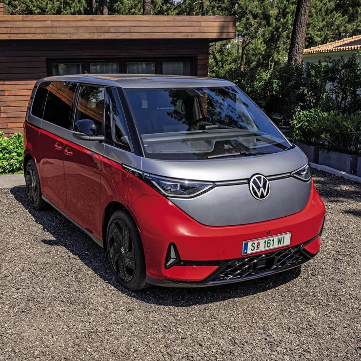 Eine Person steht neben einem roten Volkswagen ID. Buzz GTX, der in einer gepflasterten Einfahrt vor einem modernen Haus geparkt ist.