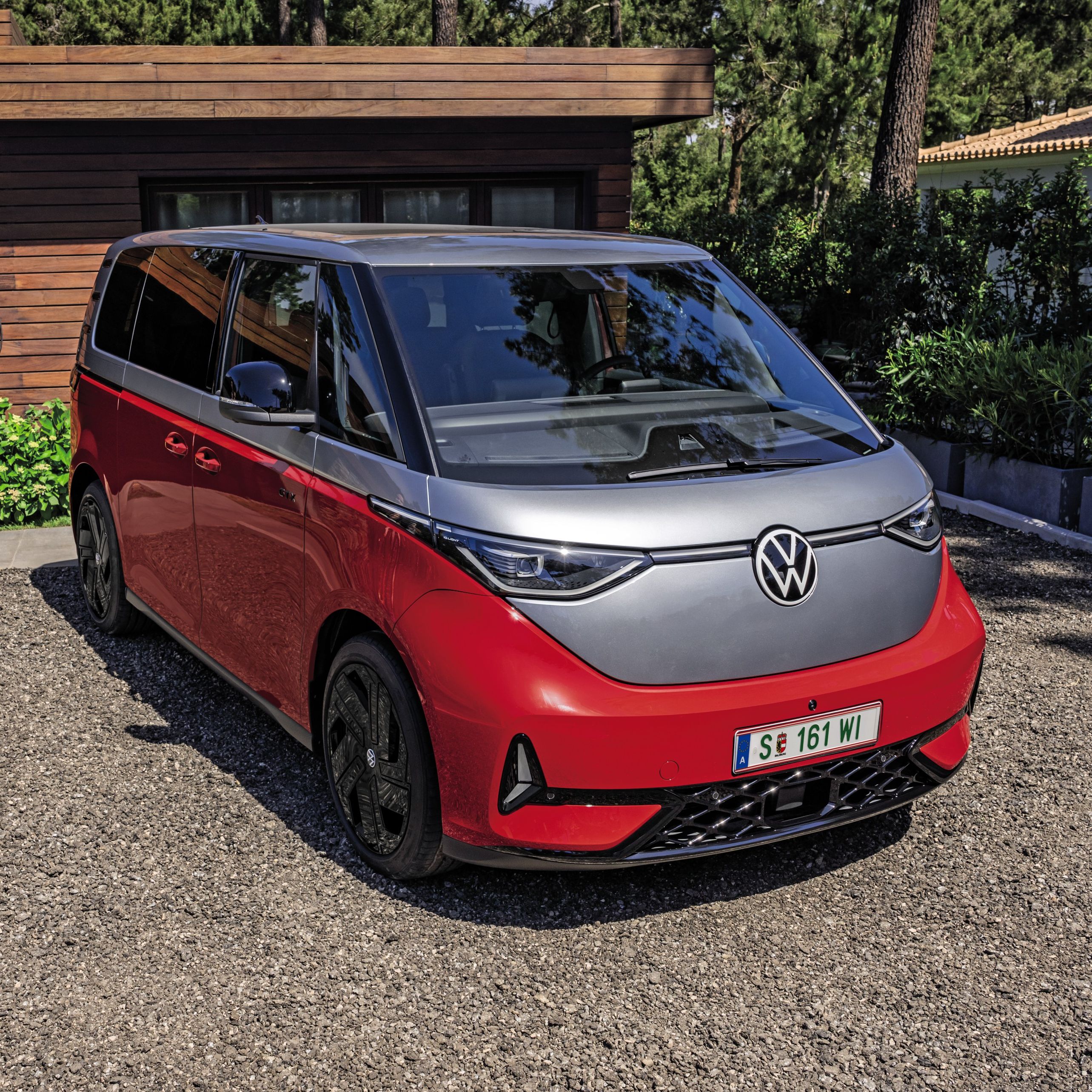 Eine Person steht neben einem roten Volkswagen ID. Buzz GTX, der in einer gepflasterten Einfahrt vor einem modernen Haus geparkt ist.