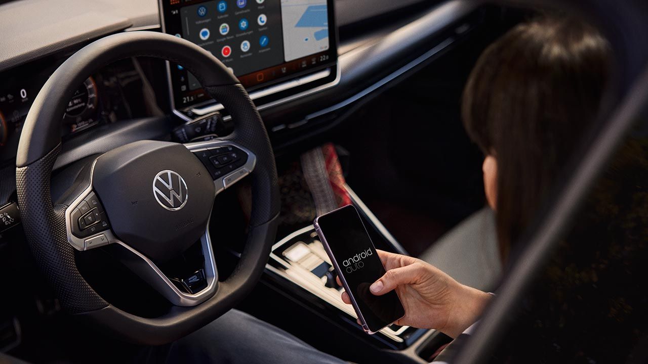 Eine Frau sitzt auf dem Fahrersitz eines VW Golf und bedient ihr Handy.