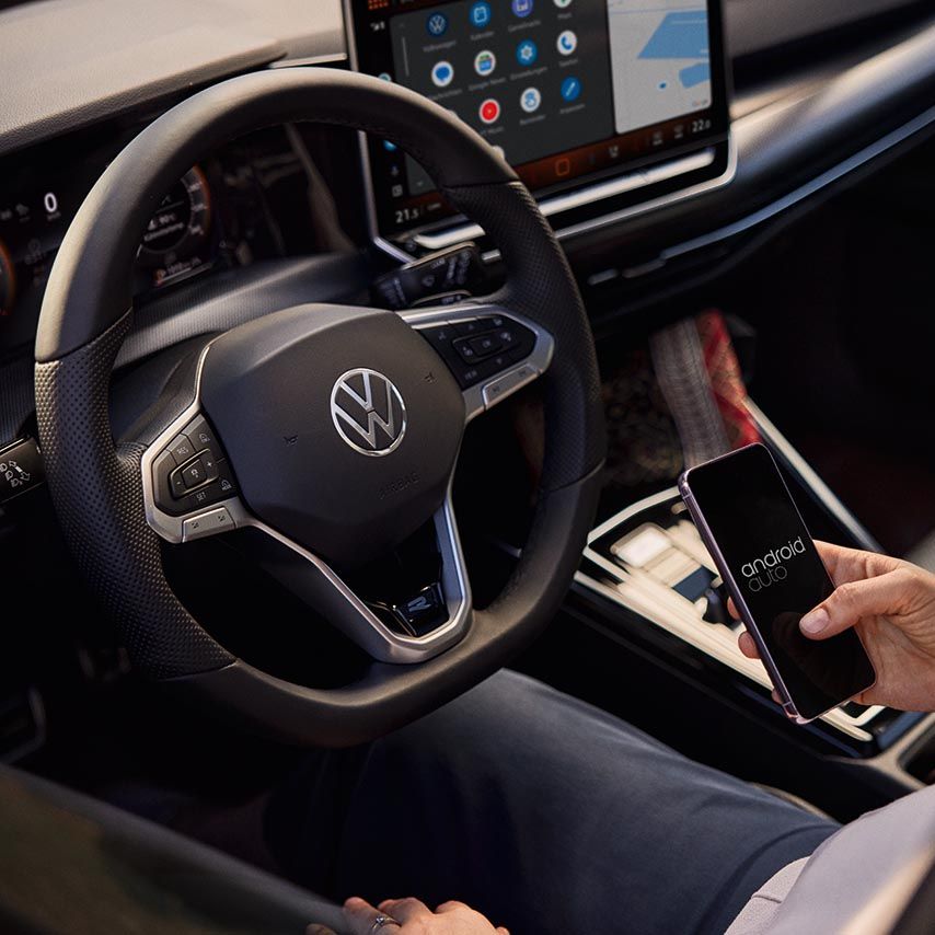 Eine Frau sitzt auf dem Fahrersitz eines VW Golf und bedient ihr Handy.