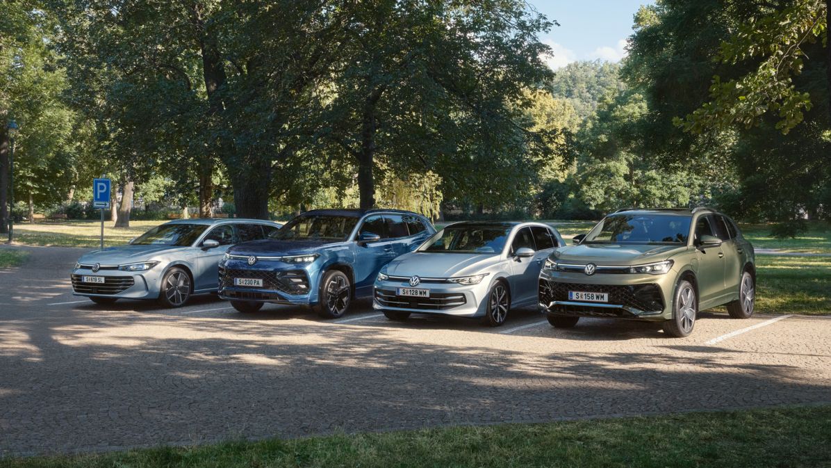 Vier VW Plug-In-Hybrid-Modelle stehen nebeneinander auf einem Parkplatz in einem Park.