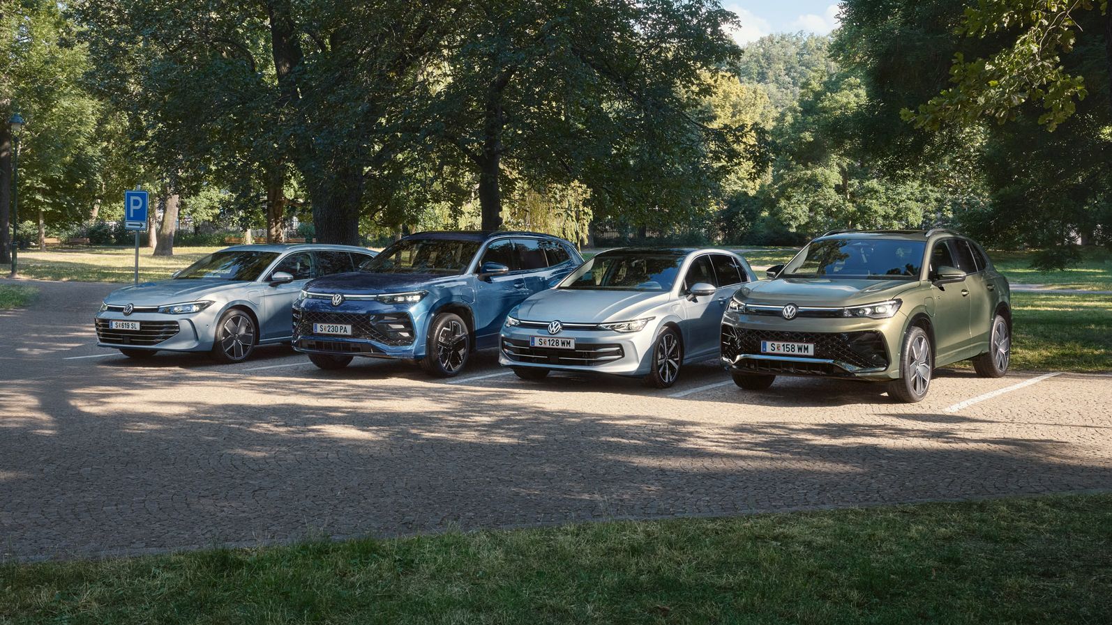 Vier VW Plug-In-Hybrid-Modelle stehen nebeneinander auf einem Parkplatz in einem Park.