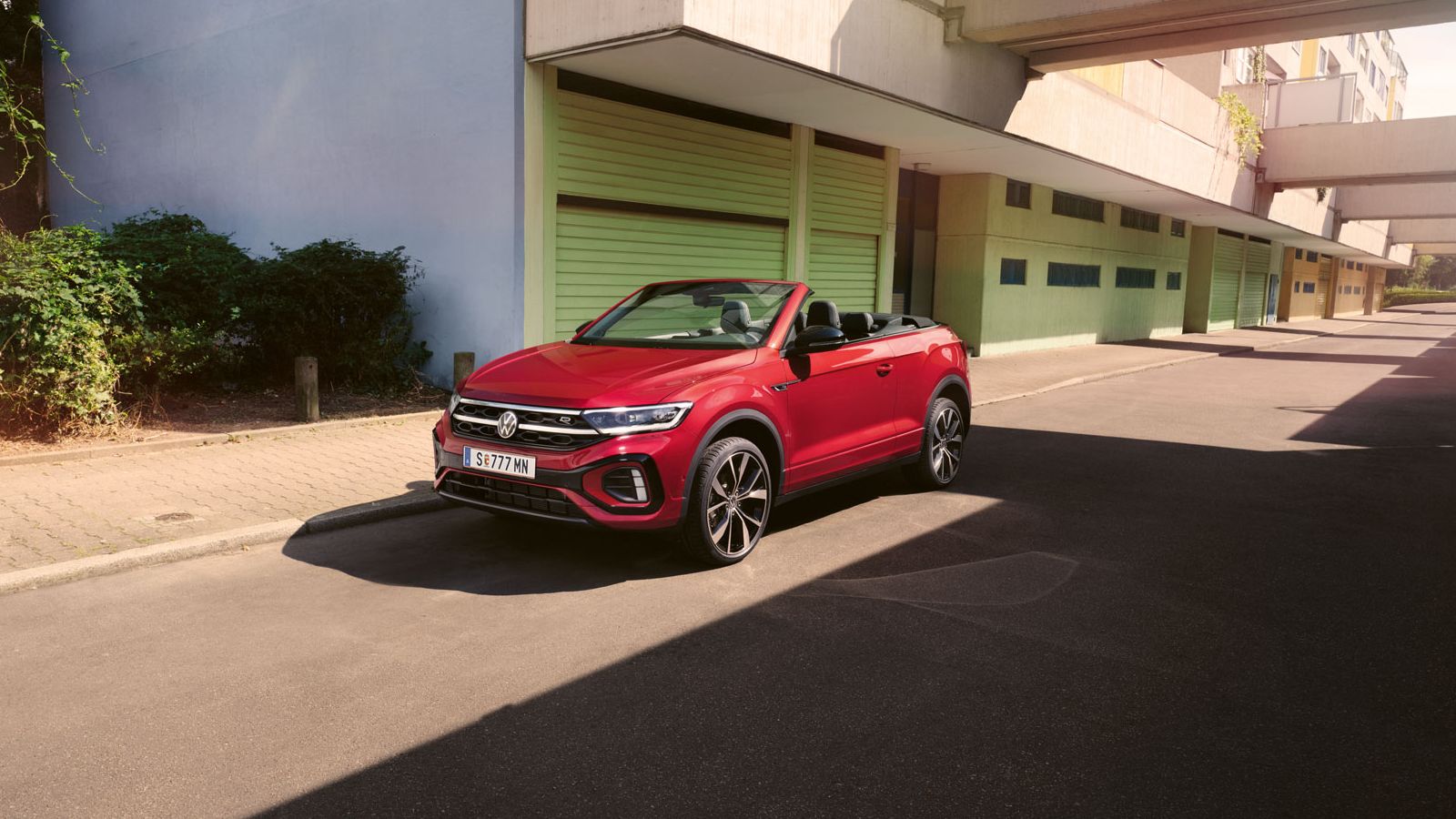 Roter T-Roc Cabriolet steht geparkt am Straßenrand neben dem Gehsteig in einer Stadt.