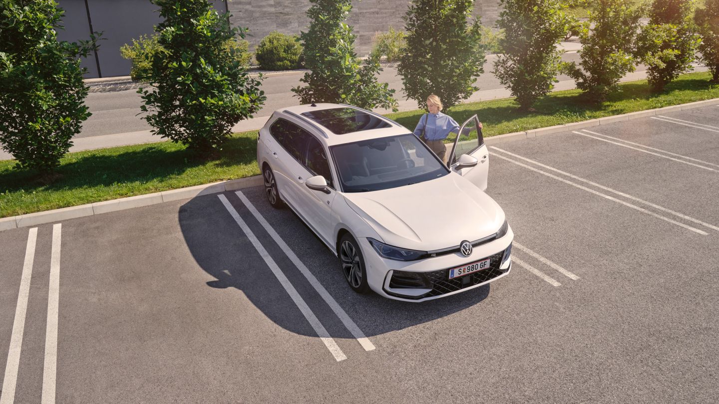 Weißer VW Passat parkt vor einem modernen Bürogebäude. Eine Frau steigt ein.