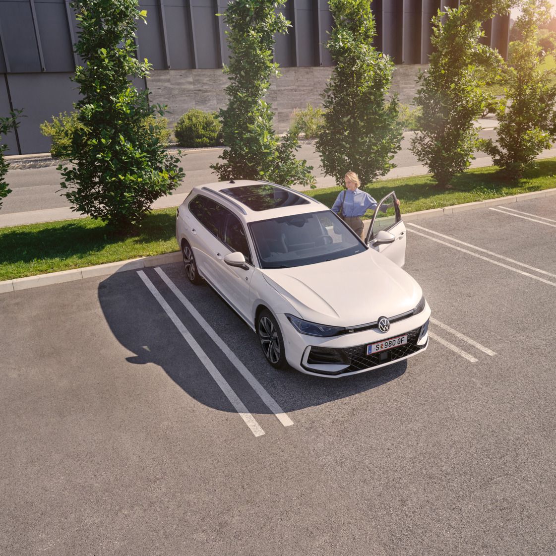 Weißer VW Passat parkt vor einem modernen Bürogebäude. Eine Frau steigt ein.