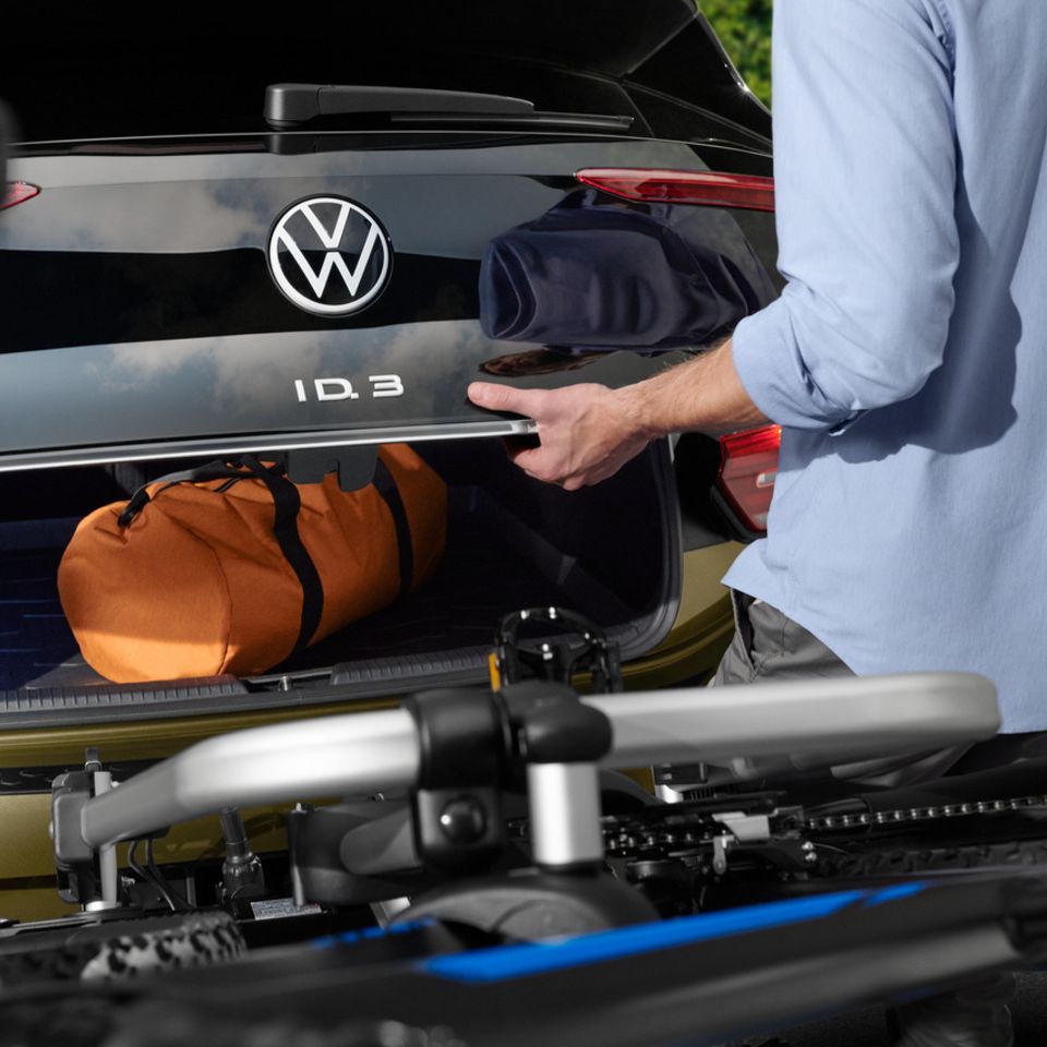 Eine Person lädt Gepäck in den Kofferraum eines ID.3 mit Fahrradträger
