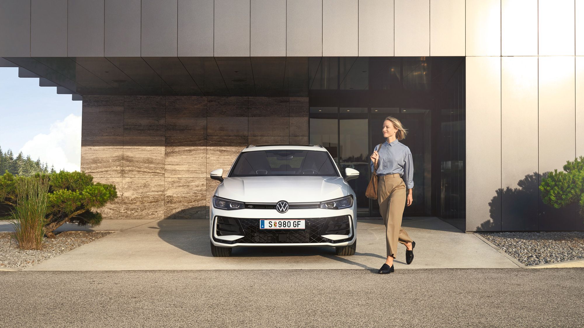 Frontansicht eines weißen VW Passat R-Line, eine Frau geht an ihm vorbei.