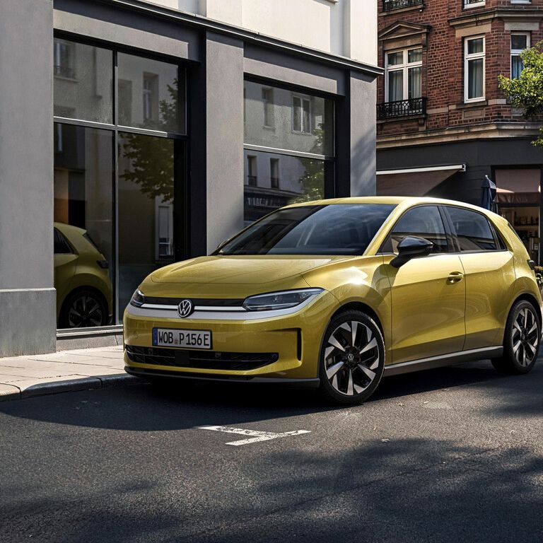 Gelber VW ID. Polo steht am Straßenrand in einer ruhigen Stadtstraße vor Schaufenstern und Altbaufassaden. Die Sonne wirft klare Schatten, wodurch die glänzende Lackierung und die schwarzen Designelemente des Autos betont werden.