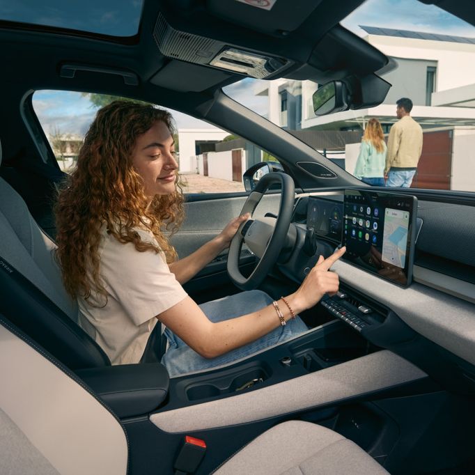 Eine junge Frau sitzt auf dem Fahrersitz eines VW ID. Cross und bedient das Infotainment-System.