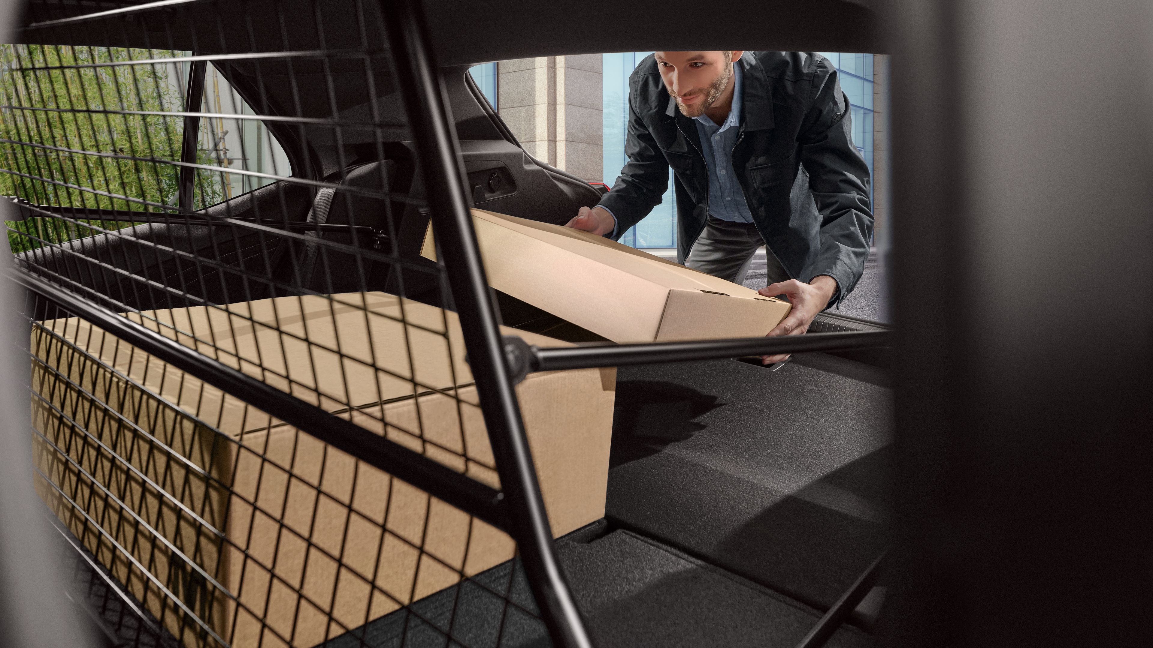 Ein Mann packt Pakete in den Kofferraum eines Volkswagen. Dieser ist mit einem Trenngitter abgeteilt.