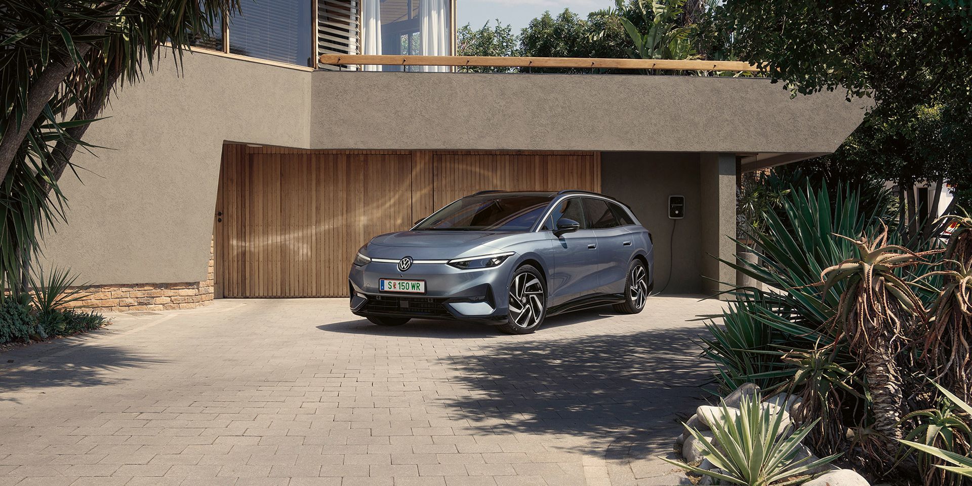 ID.7 Tourer steht geparkt vor einem modernen Haus in einer Einfahrt in Frontansicht. 