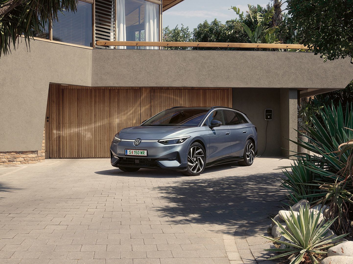 ID.7 Tourer steht geparkt vor einem modernen Haus in einer Einfahrt in Frontansicht. 