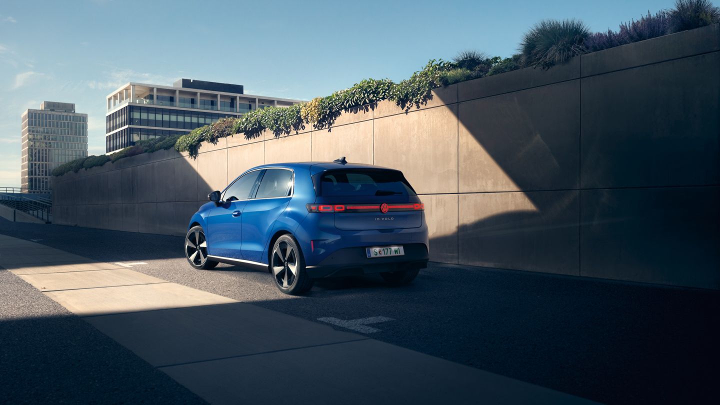 Ein blauer VW ID. Polo Style steht am Straßenrand vor einer begrünten Mauer.