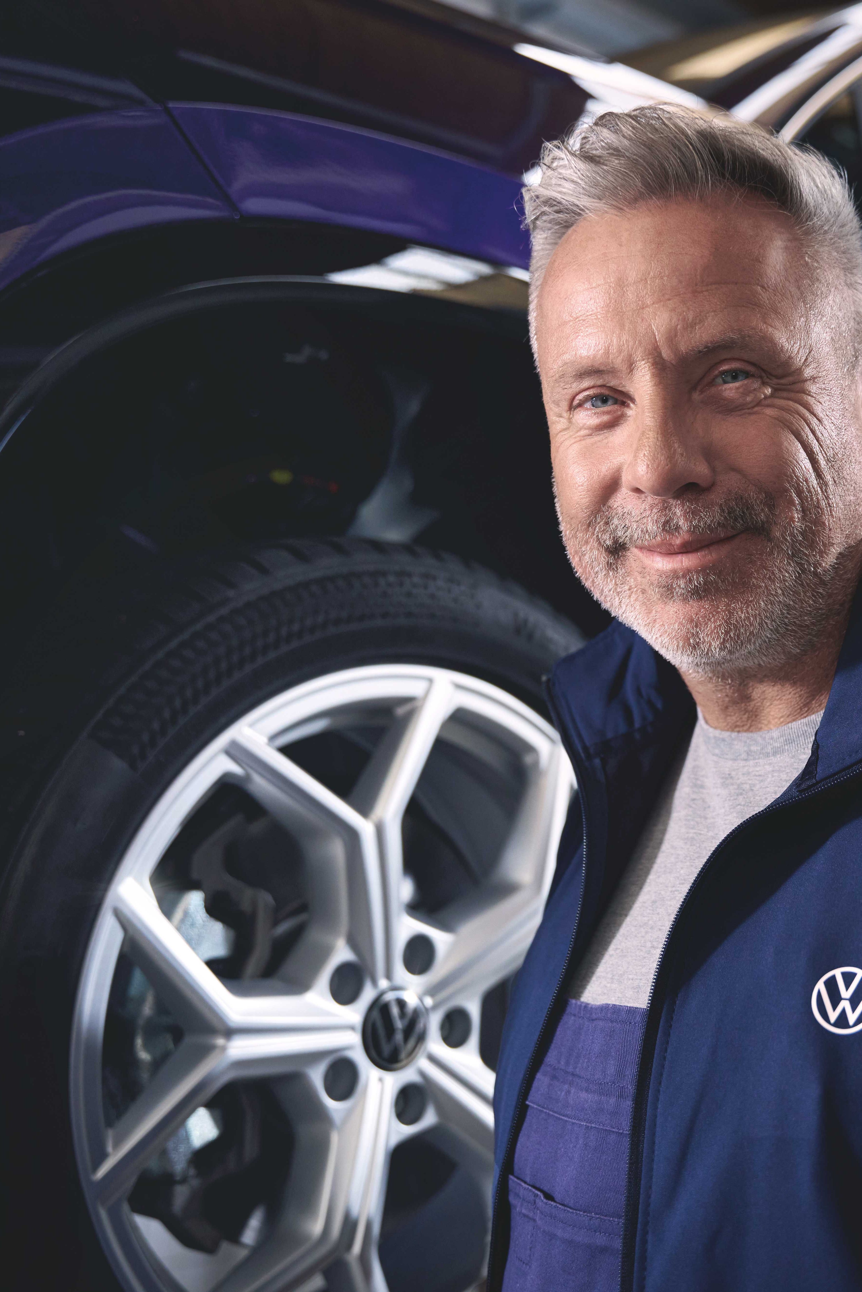 Ein Volkswagen Mechaniker vor einem blauen Volkswagen Tayron auf einer Hebebühne.