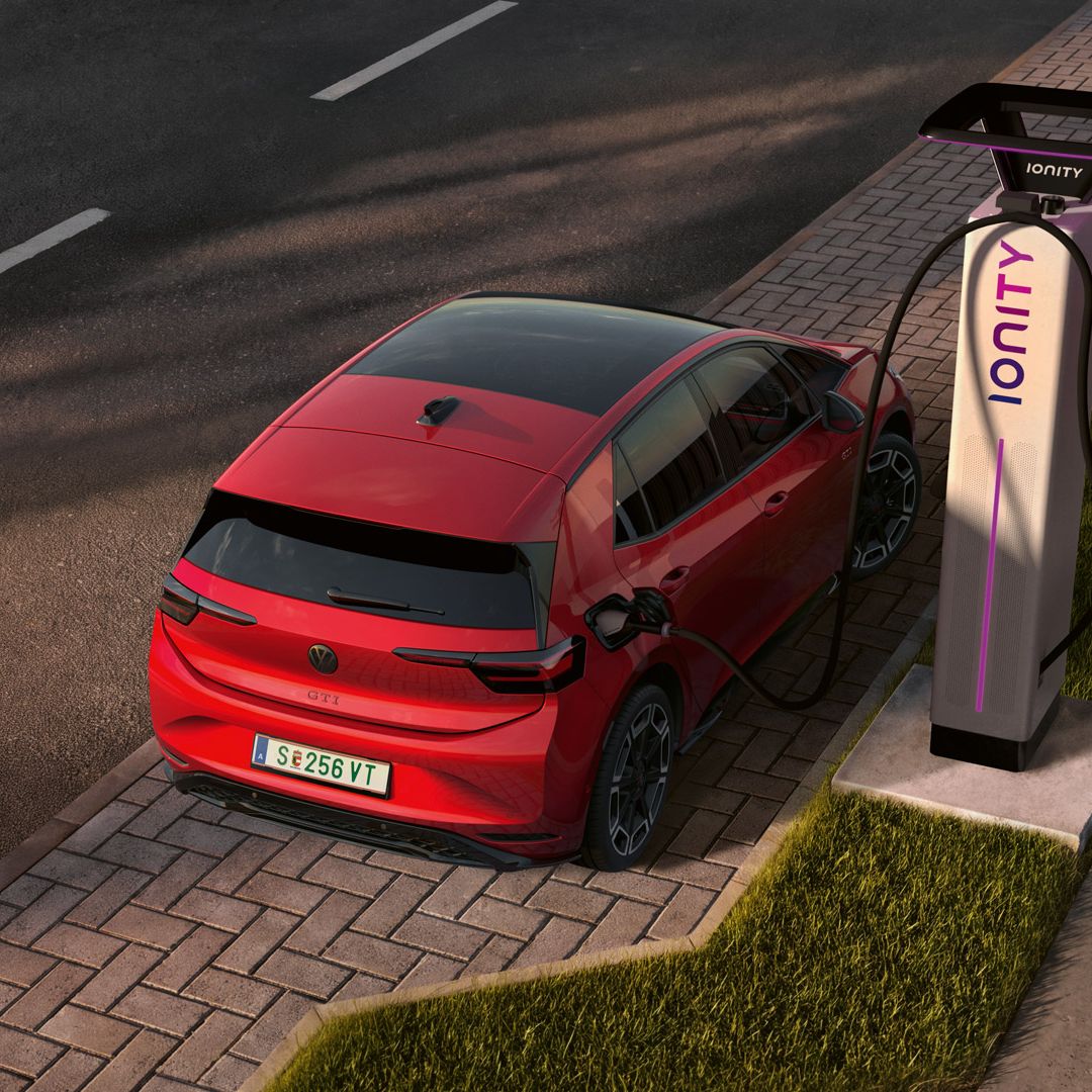 [AI-modified] – Blick von schräg oben auf den ID.3 GTI, welcher gerade am Seitenstreifen an einer Ladesäule angesteckt ist.