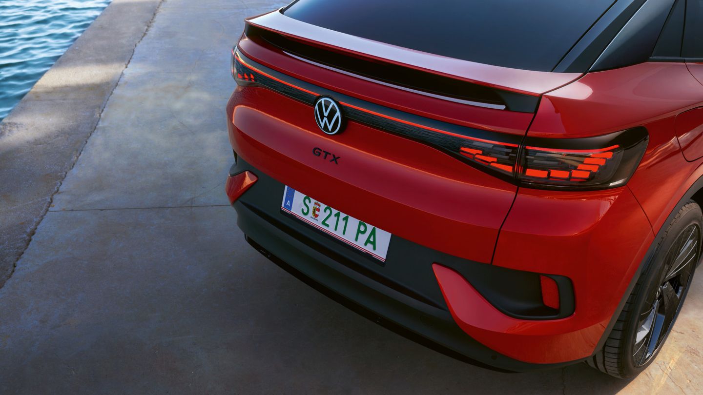 Ein rotes Volkswagen Elektroauto, Modell GTX, steht auf einer betonierten Fläche neben Wasser. Das Auto hat eine italienische Nummernschild und moderne Lichtleisten am Heck.